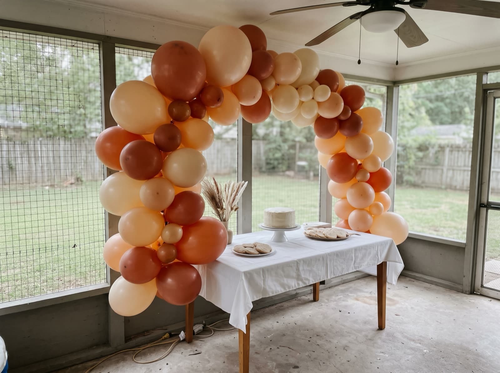 Organic balloon arch in terracotta, peach and cream over a dessert table on a screened porch