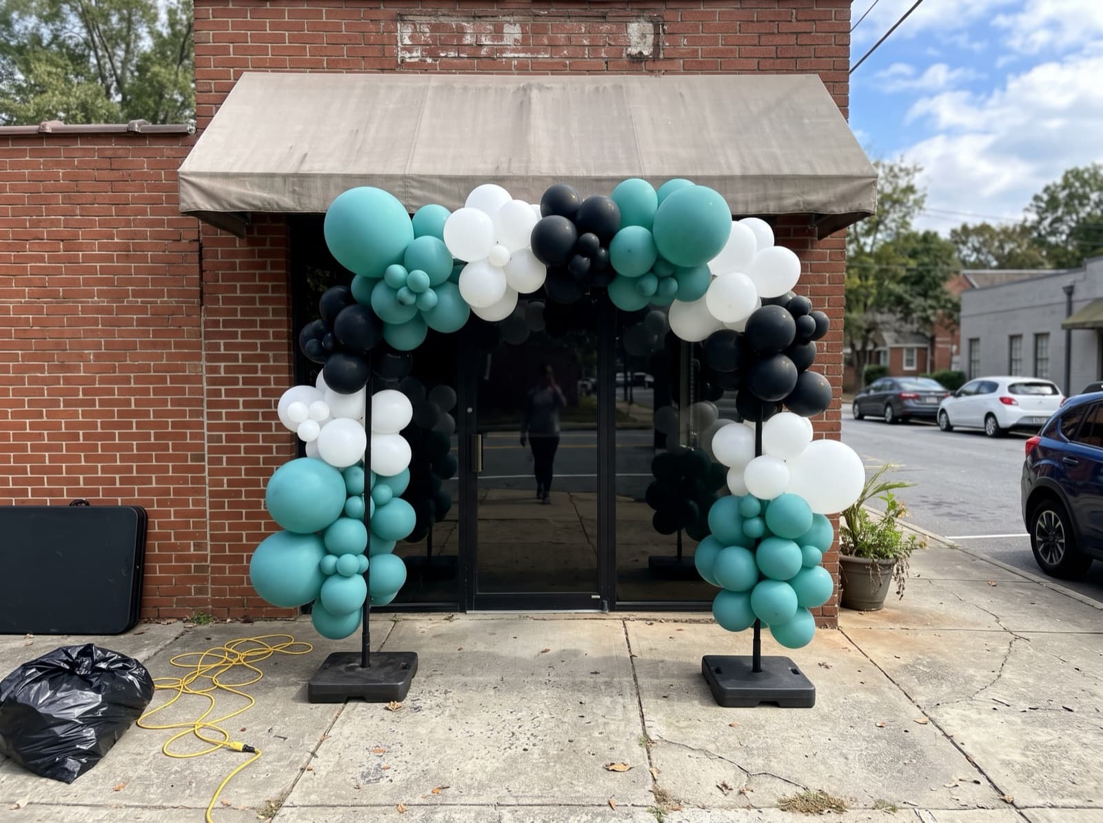 Large teal, white and black balloon arch over a shop entrance