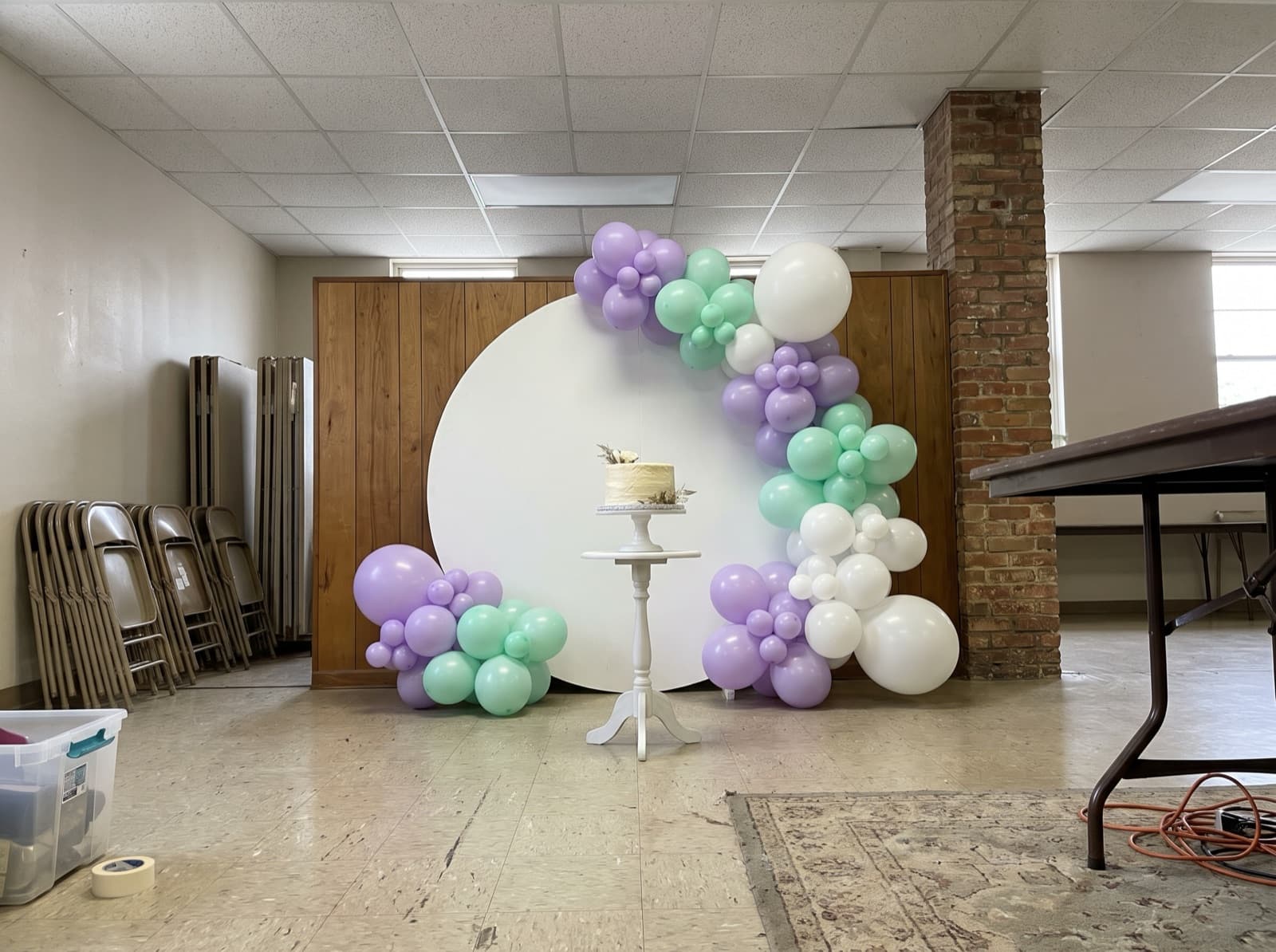 Round balloon backdrop with a lavender and mint organic garland and a cake stand in front at a birthday party