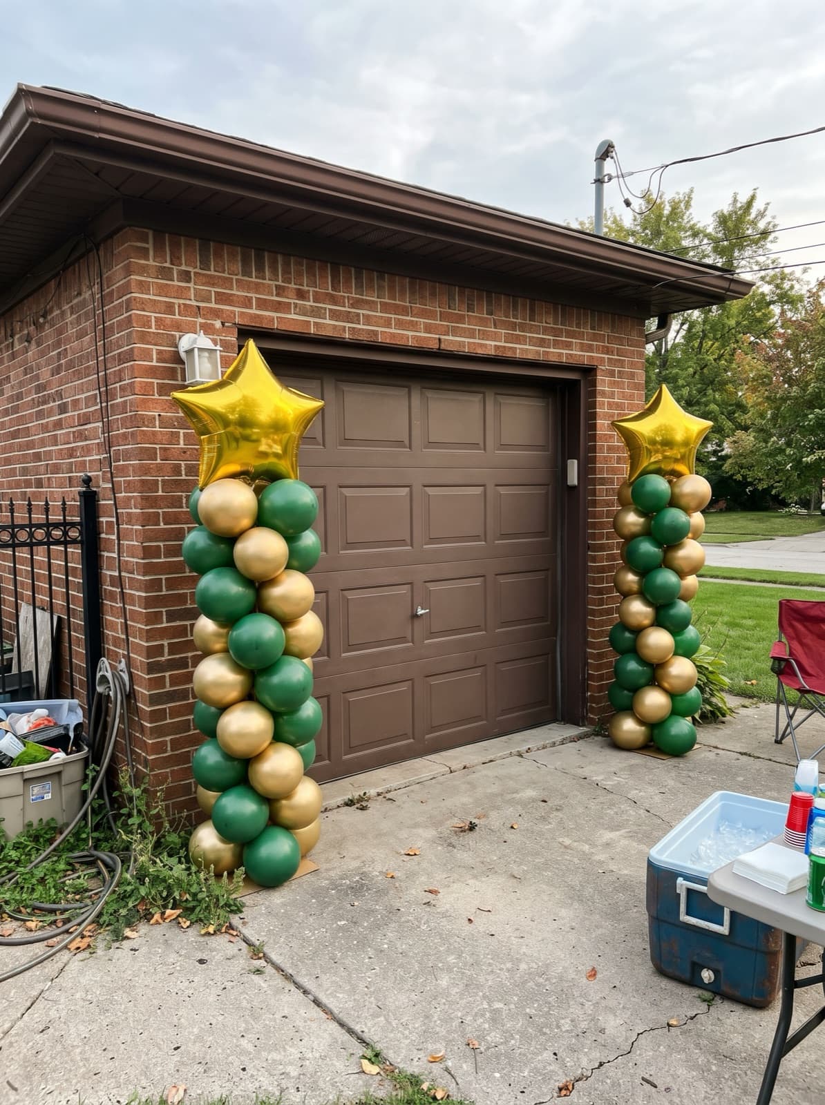 Two spiral balloon columns in green and gold with gold star toppers beside a garage door at a graduation party
